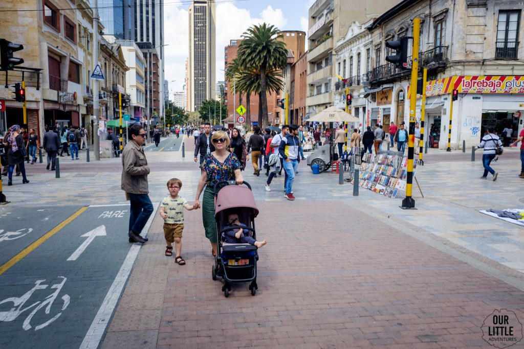 Kobieta prowadząca wózek z dzieckiem oraz trzymająca drugie dziecko za rękę na ulicach Bogoty