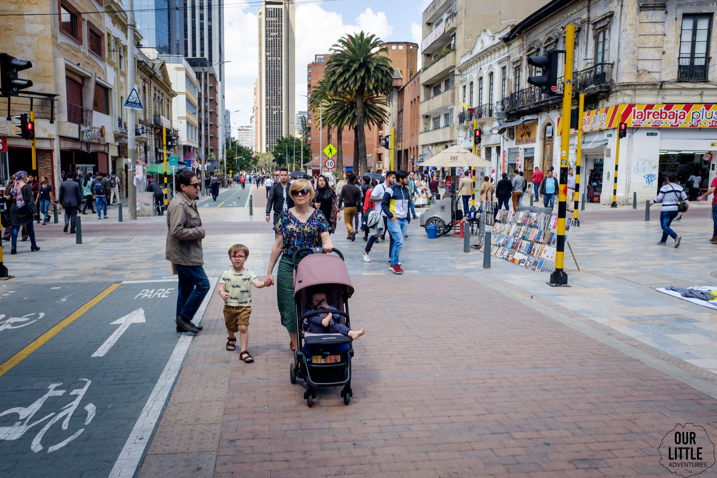 Kobieta prowadząca wózek z dzieckiem oraz trzymająca drugie dziecko za rękę na ulicach Bogoty