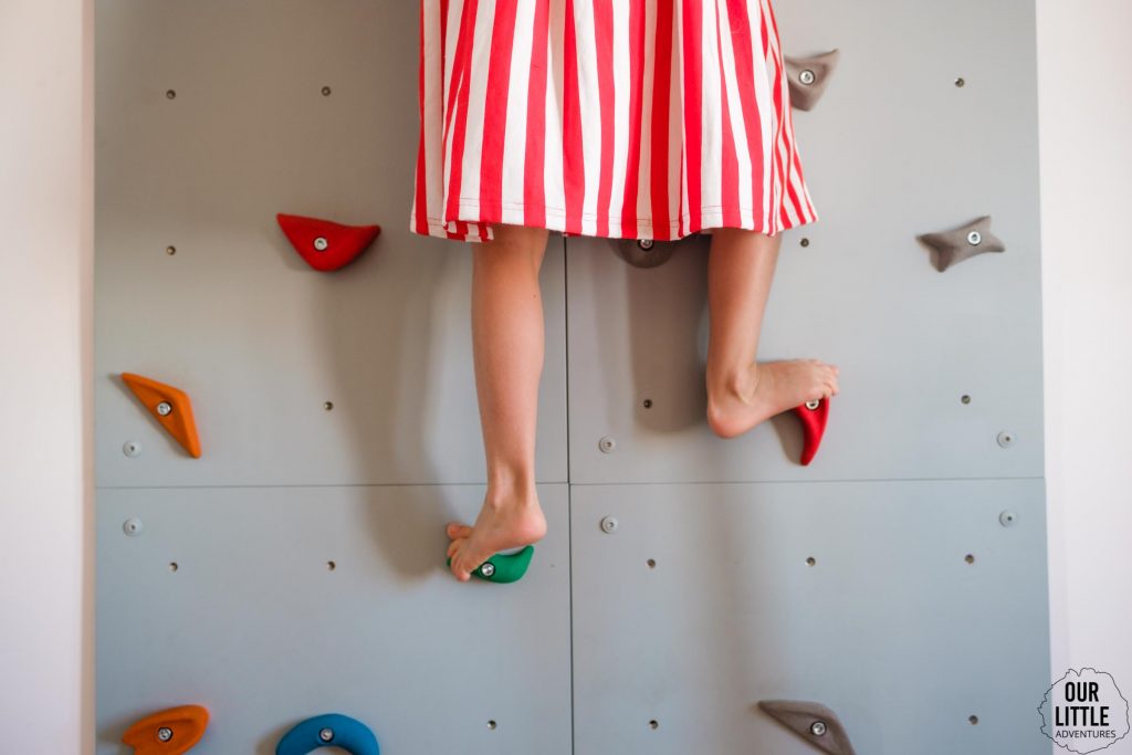 Dziewczynka w sukience w paski wchodzi na ściankę wspinaczkową. Pokój dla rodzeństwa - fot. OurLittleAdventures.pl