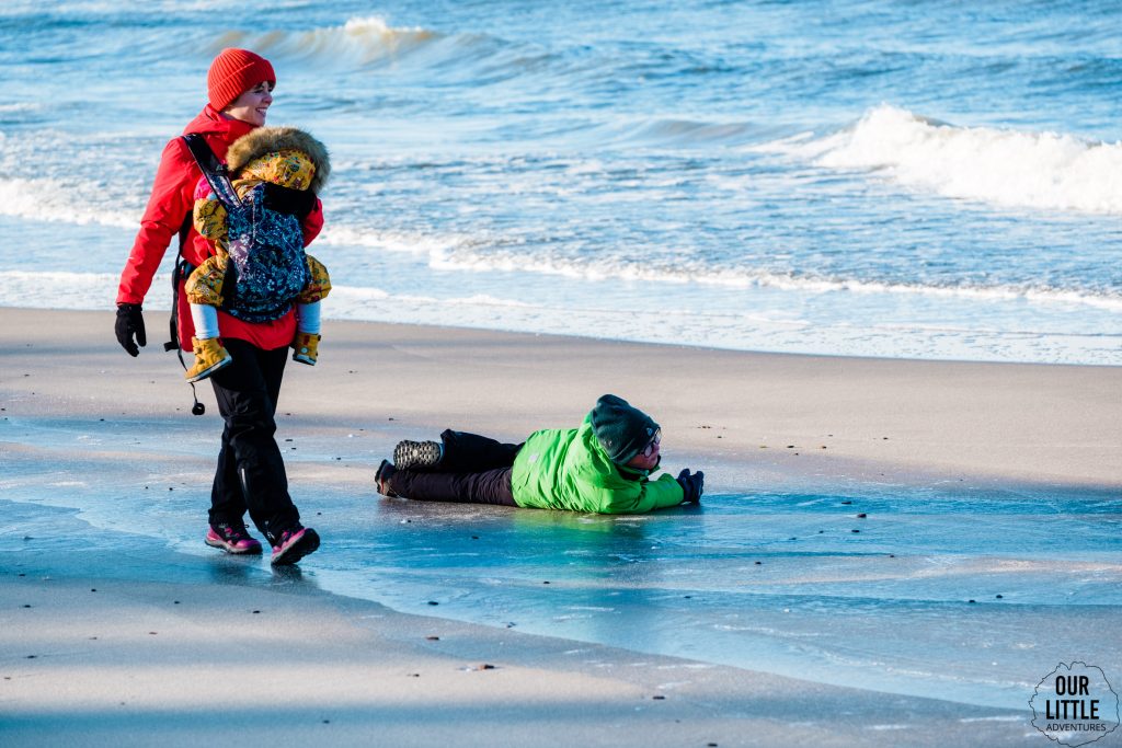 Kobieta z dzieckiem w nosidle na plaży na Mierzei Wiślanej, chłopiec leży na piasku, zdjęcie autorstwa Our Little Adventures