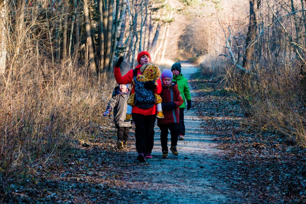 Kobieta z dzieckiem w nosidle w lesie, dzieci idą za kobietą, zdjęcie autorstwa Our Little Adventures