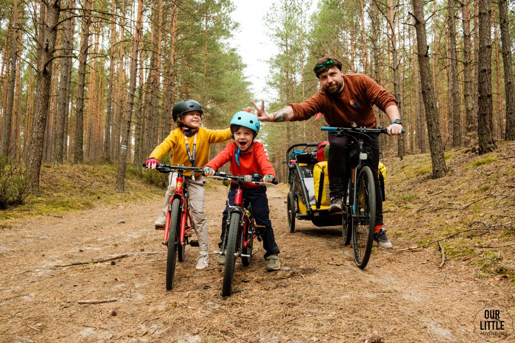 Rodzina na rowerach w lesie, tata z przyczepką, dwoje dzieci na swoich rowerach, Bory Tucholskie - Kaszubska Marszruta z dziećmi zdjęcie autorstwa OurLittleAdventures.pl