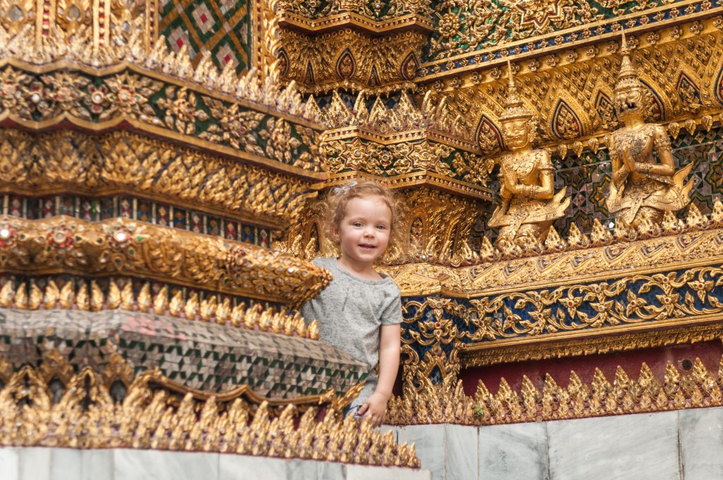 Mała dziewczynka stoi obok tajskiej świątyni, tekst: Przeprowadzka do Tajlandii, zdjęcie autorstwa OurLittleAdventures.pl