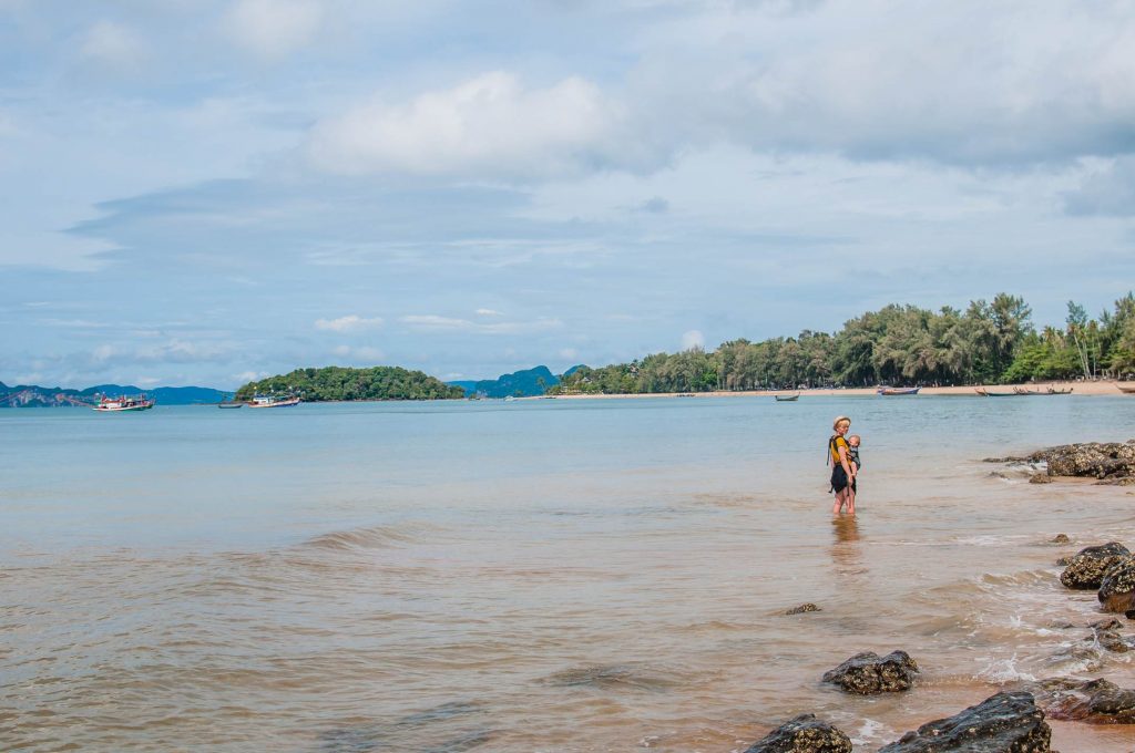 Kobieta w kapeluszu słomkowym z dzieckiem w nosidle, plaża na Krabi, tekst: Przeprowadzka do Tajlandii, zdjęcie autorstwa OurLittleAdventures.pl