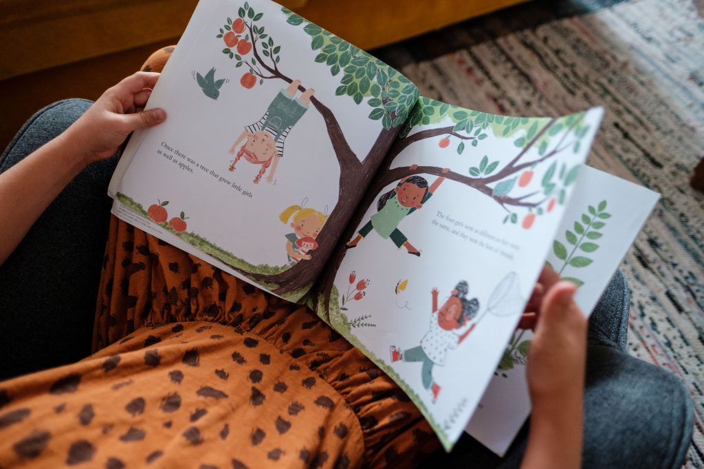 Dziewczynka siedzi na kanapie z książką, ilustracja tekstu Angielski dla dzieci, fot. OurLittleAdventures.pl
