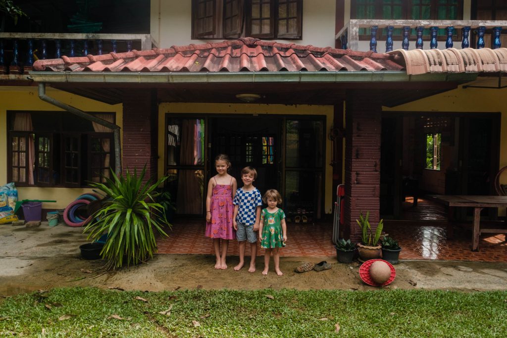 Trójka dzieci stoi przed tajską szkołą na Koh Lancie, edukacja domowa dzieci, fot. Ourlittleadventures.pl