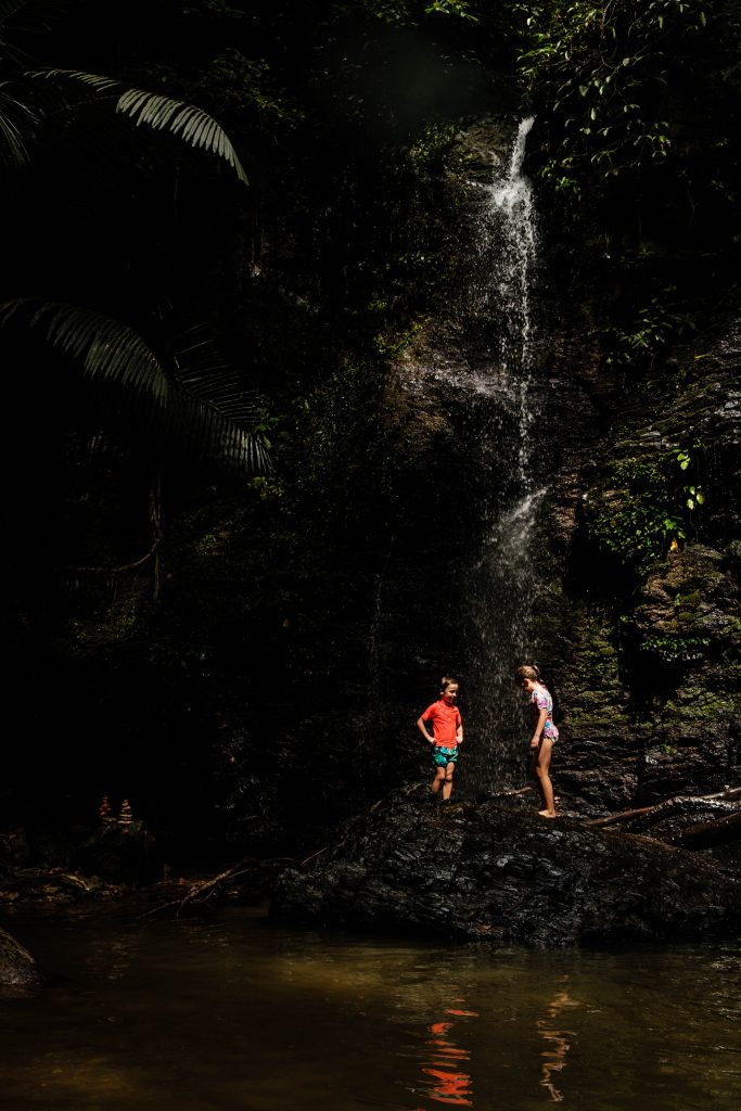 Koh Lanta - 5 powodów, aby spędzić wakacje na Koh Lancie - subiektywny przewodnik po wyspie, zdjęcie OurLittleAdventures.pl, na którym dwoje dzieic stoi pod wodospadem w lesie tropikalnym