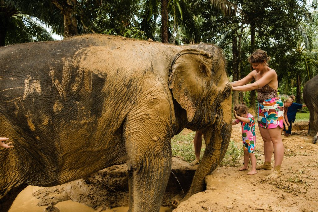 Kobieta z dzieckiem smarują słonia błotem, zdjęcie pochodzi z tekstu: Słonie w Tajlandii - dlaczego warto trochę o nich poczytać, zanim się je odwiedzi?, OurLittleAdventures.pl