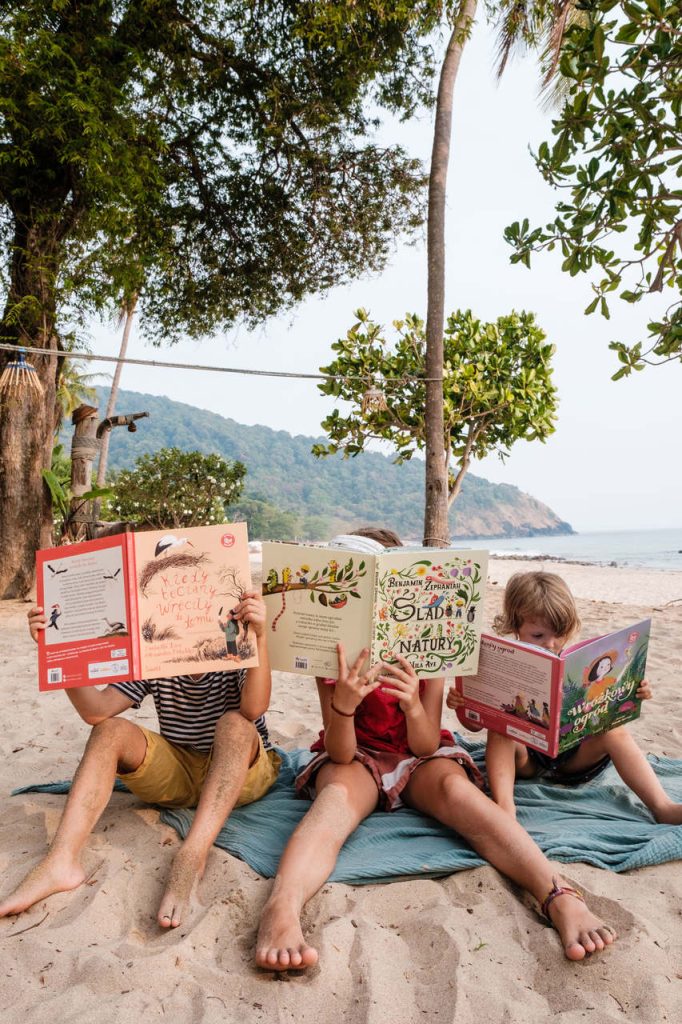 Książki z serii BLISKO NATURY wydawnictwo Świetlik trzymane przez dzieci siedzące na piasku, zdjęcie pochodzi ze strony OurLittleAdventures.pl - książki przyrodnicze dla dzieci