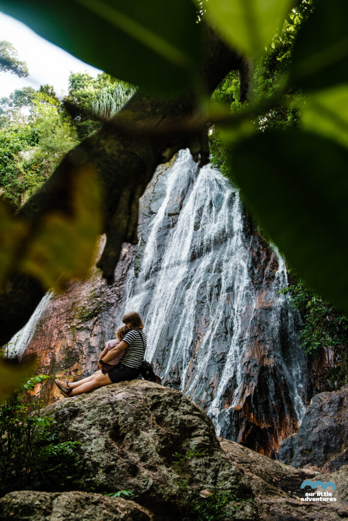 Kobieta tuli dziecko na tle wodospadu Na Muang Waterfalls na wyspie Koh Samui w Tajlandii;  zdjęcie pochodzi z tekstu Koh Samui co warto zobaczyć - 5 miejsc, tekst z bloga Ourlittleadventures.pl