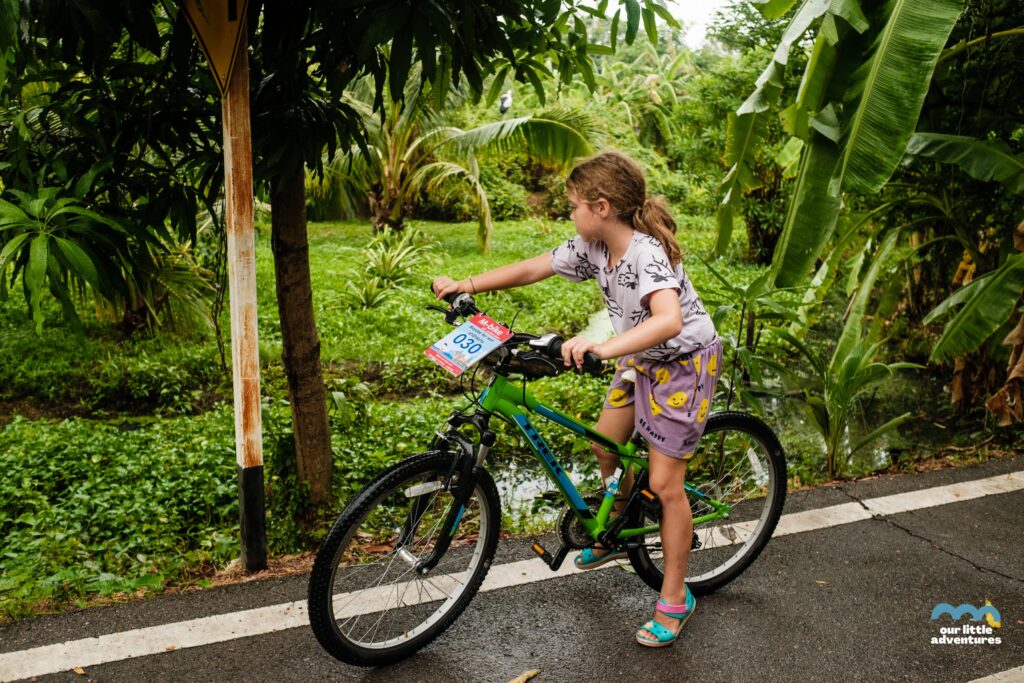 Dziecko jadące na rowerze po ulicy w Bang Kraczao w Bangkoku - zdjęcie pochodzi z tekstu na blogu OurLittleAdventures.pl pt. Wyspa Bang Krachao - wycieczka rowerowa z dziećmi do zielonej oazy Bangkoku
