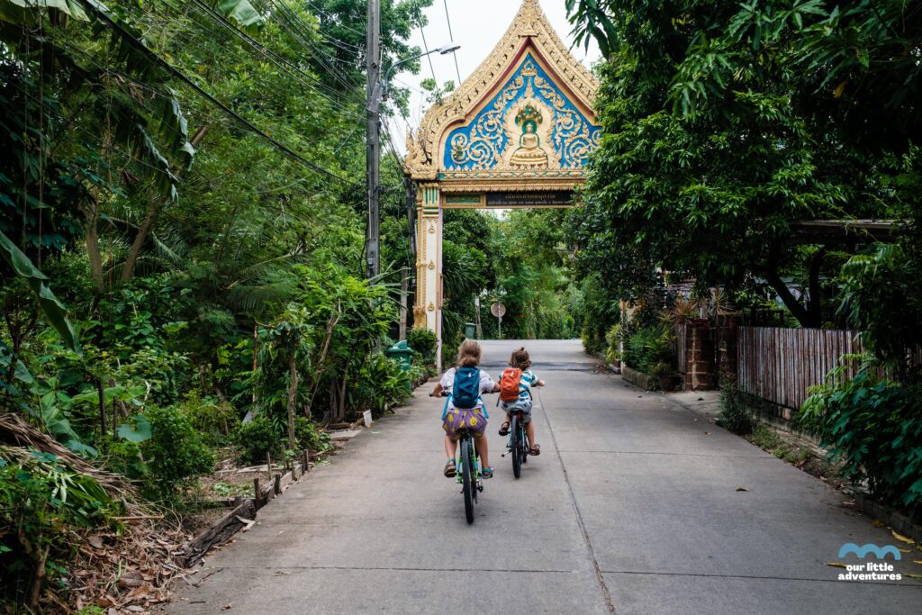 Dzieci jadąde na rowerach wzdłuż ulicy w Azji - zdjęcie pochodzi z tekstu na blogu OurLittleAdventures.pl pt. Wyspa Bang Krachao - wycieczka rowerowa z dziećmi do zielonej oazy Bangkoku
