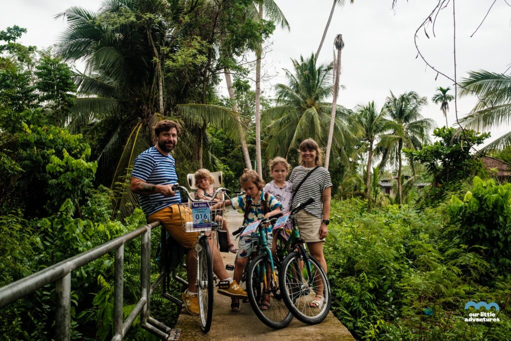 Rodzina z dziećmi na rowerach na wąskiej kładce rowerowej w Azji - zdjęcie pochodzi z tekstu na blogu OurLittleAdventures.pl pt. Wyspa Bang Krachao - wycieczka rowerowa z dziećmi do zielonej oazy Bangkoku