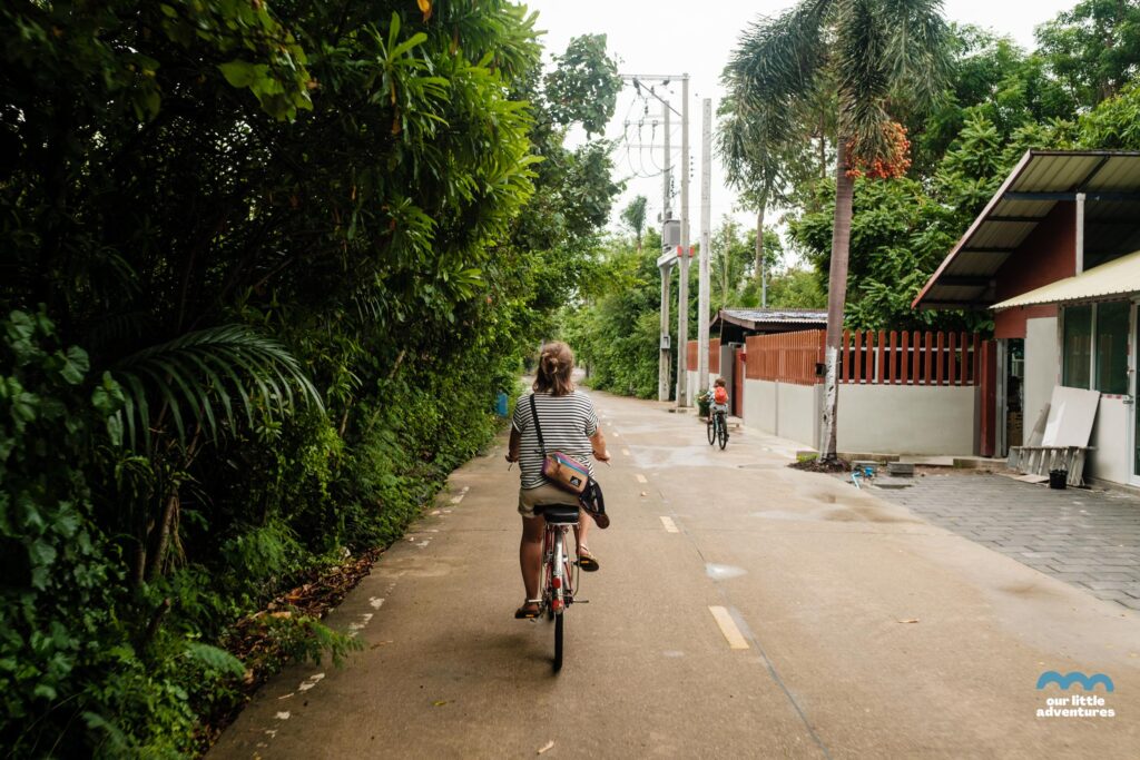 Kobieta jadąca na rowerze wzdłuż ulicy w Azji - zdjęcie pochodzi z tekstu na blogu OurLittleAdventures.pl pt. Wyspa Bang Krachao - wycieczka rowerowa z dziećmi do zielonej oazy Bangkoku