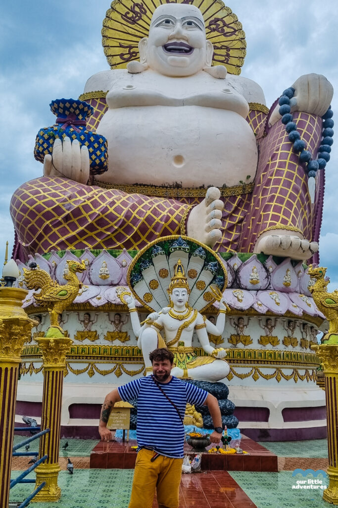 Mężczyzna na tle posągu Buddai w Świątyni Wat Plai Laem na wyspie Koh Samui w Tajlandii,  zdjęcie pochodzi z tekstu Koh Samui co warto zobaczyć - 5 miejsc, tekst z bloga Ourlittleadventures.pl